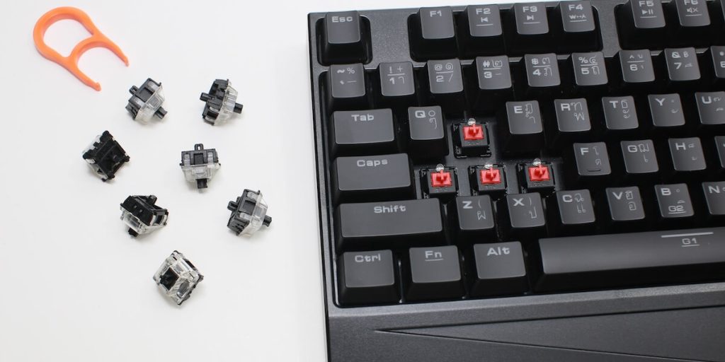 Mechanical keyboard with WASD keycaps missing, next to switches and a puller.