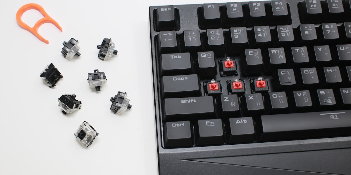 Mechanical keyboard with WASD keycaps missing, next to switches and a puller.